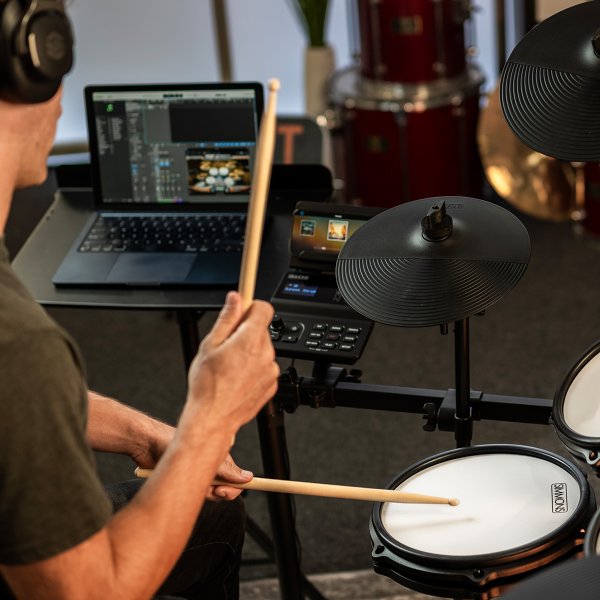 Drummer playing a drum set indoor, with electronic cymbals and drumsticks in motion